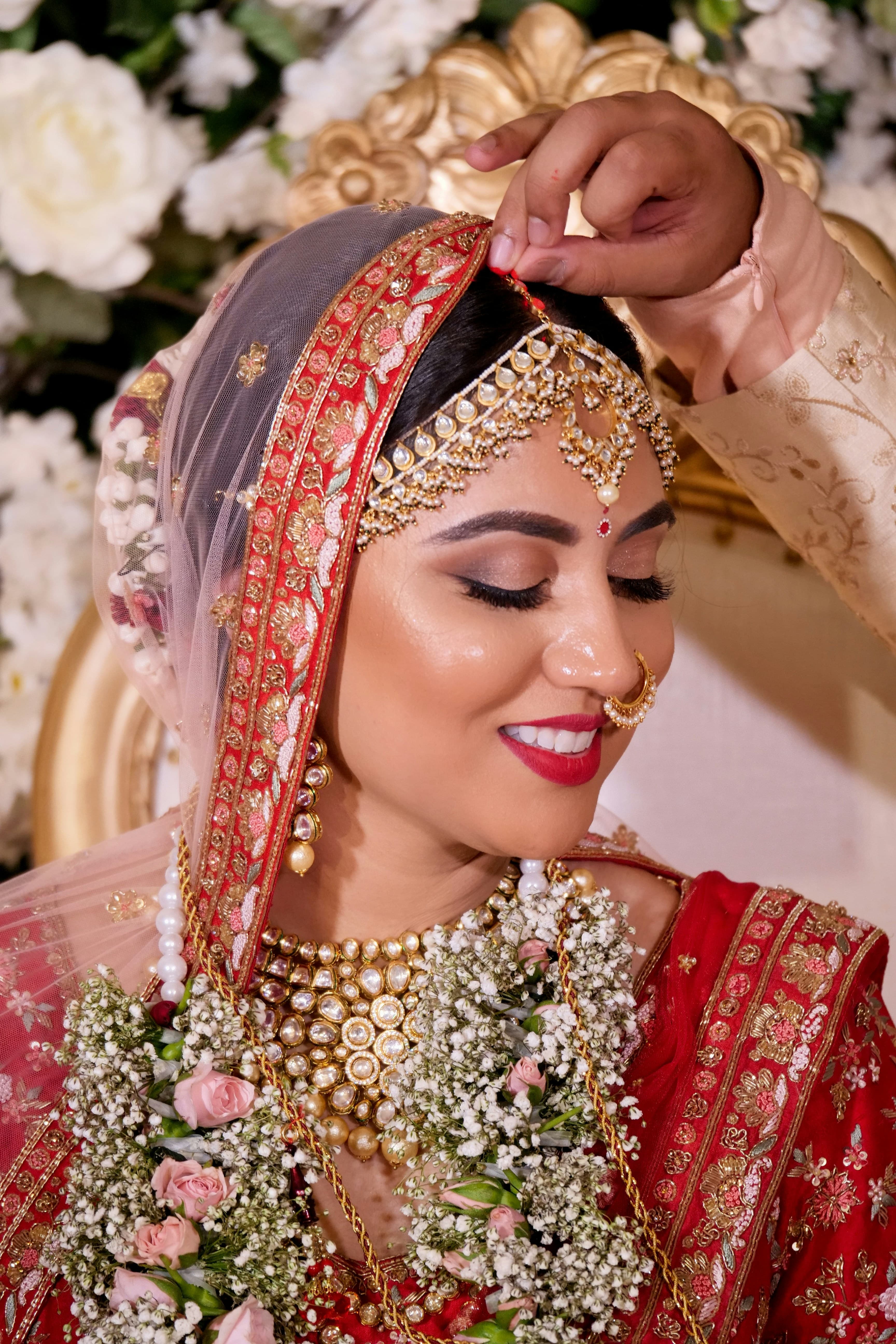 Smiling bride in red having her matha patti adjusted